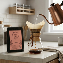 Load image into Gallery viewer, Pouring hot water from a copper kettle into a glass Chemex coffee maker with a paper filter, set on a kitchen counter next to a bag of Ethiopia Coffee roasted by No Sleep Roastery.