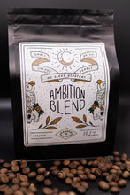 Load image into Gallery viewer, A black coffee bag labeled Ambition Blend by No Sleep Roastery, with roasted coffee beans scattered in front on a dark background.
