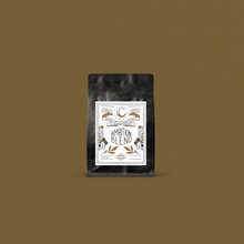 Load image into Gallery viewer, Fresh roasted coffee in a black bag with a designer label displayed on a bronze background