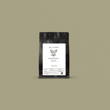 Load image into Gallery viewer, Fresh roasted coffee in a black bag with a white label displayed on a sage background