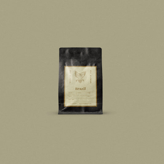 A single black coffee bag package with a cream-colored label stands centered against a solid muted olive-beige background. The label features a stylized owl logo.