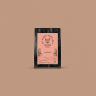 Fresh roasted coffee in a black bag with a pink label displayed on a light brown background