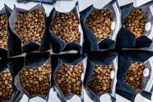 Load image into Gallery viewer, Close-up of coffee beans in black bags with a reflective surface.
