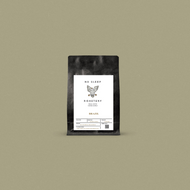 Fresh roasted coffee in a black bag with a white label displayed on a sage background